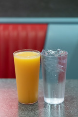 Two Glasses one full of Orange Juice and One full of Iced water in a Diner