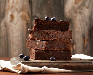stack of square baked slices of brownie chocolate cake with walnuts on a wooden surface