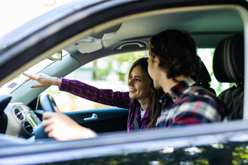 Young man driving car pointing something interesting to his girlfriend. Caucasian couple on summer...