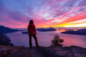Adventurous Caucasian Girl standing on top of a mountain during a colorful winter sunset. Taken on...