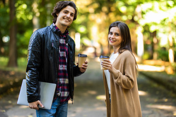 Photo of young loving couple students outdoors outside at street walking drinking coffee talking with each other.