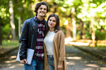 Young attractive couple of man and woman walking in urban city center talking, working together, smiling, stylish freelance people, holding laptop discussing