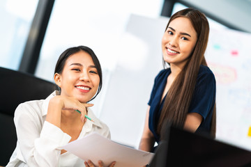 Portrait of two beautiful Asian office coworkers smiling together at work. Business colleagues, teamwork partner, job consultant, or working woman concept