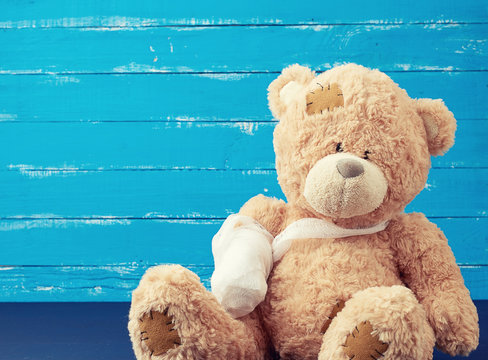 brown teddy bear with rewound white bandage paw on a blue wooden background