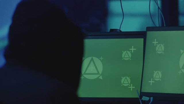 Man in the cap is sitting and working on stealing data at the computer as haker. Hideout Place has Dark Atmosphere.