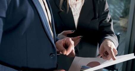 Close up man and a woman discussing work in the brightly lit modern office. Concerned male and female working with charts papers at hands. Standing business people discuss new startup project concept