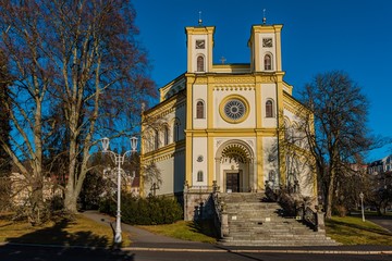 Fototapeta na wymiar Marianske Lazne, Czech Republic - January 1 2020: View of the Christian church of Assumption of Virgin Mary with two towers on a sunny winter day. Trees and green grass in a park around.