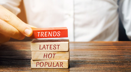 Businessman puts wooden blocks with the words Trends, latest, hot, popular. Popular and relevant topics. New ideological trends. Recent and latest trend. Evaluation methods. - obrazy, fototapety, plakaty