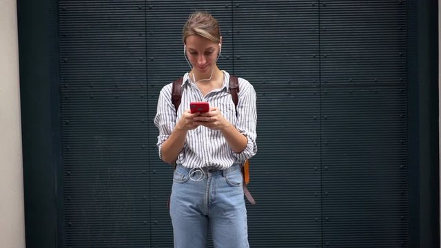 Slow motion effect of positive hipster girl enjoying favorite songs in modern headphones, female tourist listening music and messaging on website via phone device