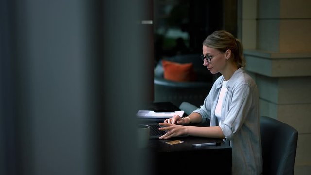 Skilled female remote worker typing report on laptop computer analyzing information rereading text from laptop, woman in eyewear making booking online on organizing job connected to wifi