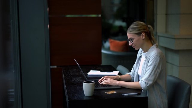 Caucasian woman typing text request on laptop computer for searching information on website using internet connection, positive hipster girl working remotely at modern netbook