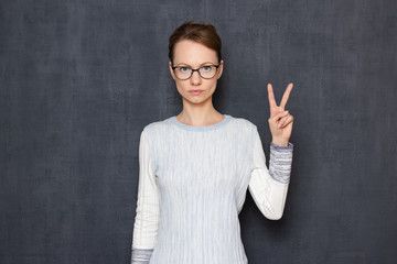 Portrait of serious focused young woman showing peace gesture