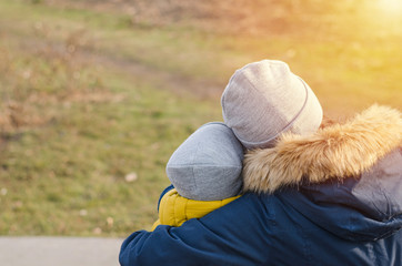 Mother hugs child on wooden bench. Care and love.