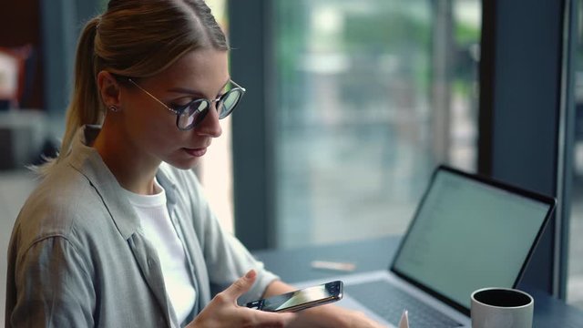 Skilled female manage director doing paperwork sitting next to desktop with modern laptop computer, business woman making photos of some financial documents using smartphone camera