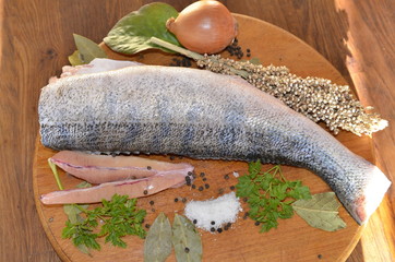 On a wooden board lies fresh pike perch fish fillet, yellow lemon, onion, salt, herbs, spices.