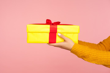 Closeup of female hands in warm sweater holding wrapped yellow gift box with stripe, arms giving...