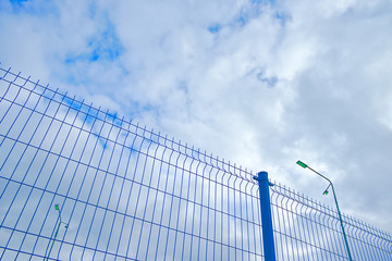 clouds in the blue sky and part of the mesh fence
