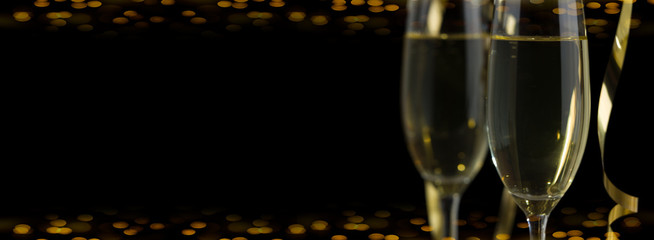 Two glasses of champagne in front of panoramic yellow bokeh black background