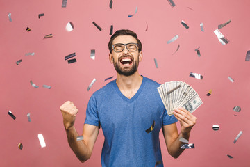 Happy winner! Young rich man in casual t-shirt holding money dollar bills with surprise isolated...