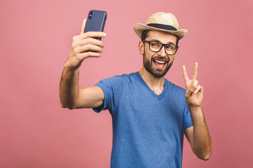 Travel concept. Portrait of cheerful young man in straw hat taking selfie with smartphone isolated...
