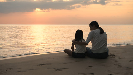Fototapeta premium Holiday concept. Mother and daughter are watching the sunset on the beach. 4k Resolution.