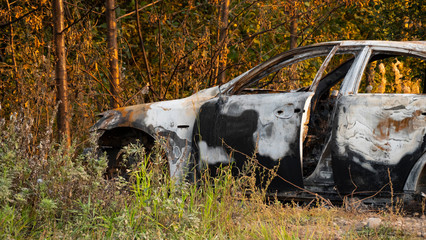 The car after the fire. Burned out engine. Burnt car without a hood, ash and garbage after a fire. Arson of a car near a forest near the city. Traffic accident and vandalism concept. 