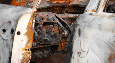 Burnt out car. Burnt passenger car near the city by the forest. Burnt door and car interior ,Close up. Rusty, steel case and wheels. The concept of a traffic accident and vandalism or crime.