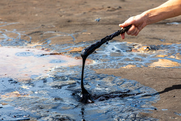 A man's hand stirring liquid asphalt with a wooden stick at Pitch Lake, the largest natural deposit of bitumen in the world. La Brea, Trinidad island, Trinidad and Tobago