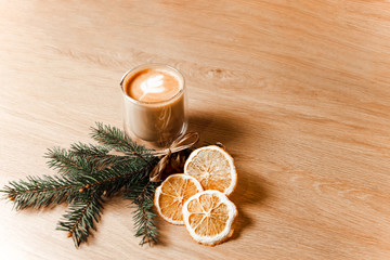 Composition of a cup of latte, coffee beans, dried oranges and a fir branch. 