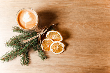 Composition of a cup of latte, coffee beans, dried oranges and a fir branch. 