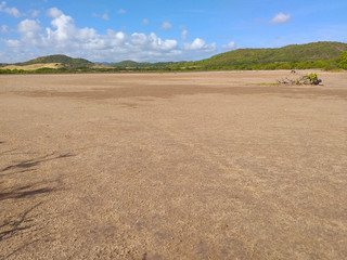 Fototapeta na wymiar Panoramic photo of dry salt pans of ocher color. Blue sky with tropical clouds and mountains with vegetation. Martinique, French West Indies.