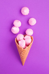 Ice cream cone with pink meringue  in the center of the violet  background. Top view. Copy space. Location vertical.