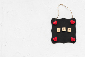 ILY leters as abbreviation of I love you and jelly hearts on a black board, white background, copy space. Top view, flat lay, mockup. Valentines Day concept