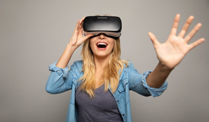 Unusual experience. Close up photo of a stunned woman in a casual outfit, who is wearing VR glasses, holding them with her right hand and stretching her left hand towards the camera.
