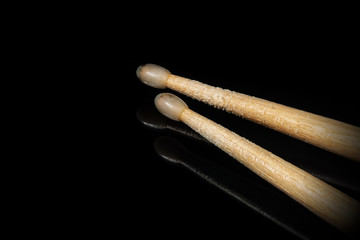 Close-up of a pair of used wooden drumsticks on a black background with reflections and copy space. Percussion instrument