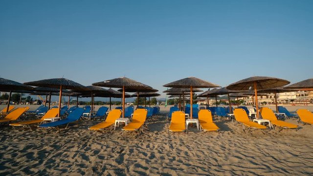 Beds and umbrellas on the empty beach in a resort at sunrise