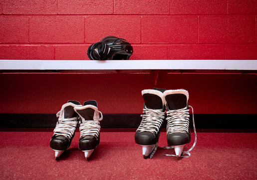 Hockey skates for adult and kids standing over floor in locker room with red background and copy space 