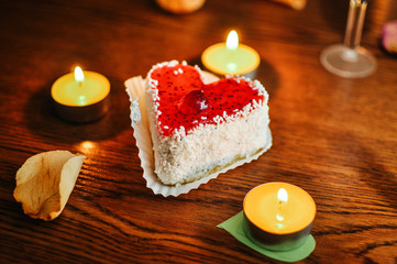Cupcake with sprinkles and heart candles on wooden background, strawberry creamy cake, red cherry on top. Yellow leaves of dried roses. Romantic cake, pie for concept St. Valentine's Day. Close Up.