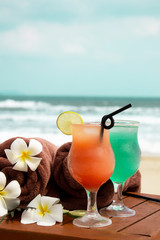 Tropical ice summer drinks and cocktails, towels and a women's straw hat on a white sandy beach on a background of blue sea. Copy space.