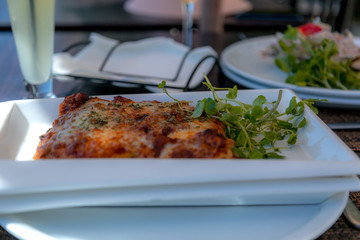 Plato de lasaña con salsa, acompañado de verdutas verdes