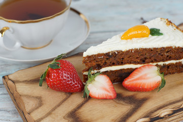 A slice of sweet carrot cake and a mug of tea next to strawberries