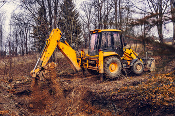 A yellow rusty industrial excavator with a bucket lying on the ground, digging the ground at a construction site in a pond forest.
