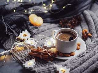 Fototapeta na wymiar Winter Breakfast. A mug of hot coffee with a scarf on the table with cinnamon, tangerines, garland. Home comfort