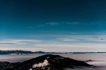 scenic view of snowy mountains with pine trees and white fluffy clouds in dark sky in evening