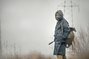 Soldier in gas mask and raincoat with a rifle walking on the empty road concept.