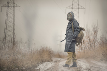 Soldier in gas mask and raincoat with a rifle walking on the empty road concept.