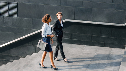 Two women in office wear walking outdoors and talking