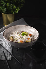Asian beef salad with cucumber, noodles and rice flakes. Thai dish on black wooden background.