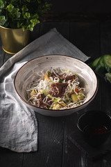 Asian beef salad with cucumber and noodles. Thai dish on black wooden background.
