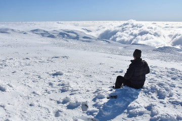 Lonely mountaineer get rest on snowy mountain high above the clouds. Happy climber enjoy in view from top of Dry Mountain, Serbia